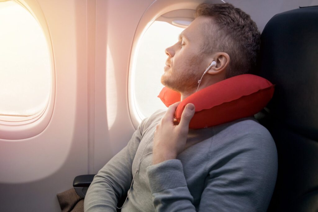 Tips to Stay Comfortable While Travelling | Elect Chauffeurs man using neck pillow on flight